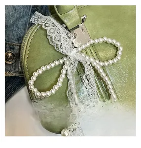 Detail der olivgrünen Handtasche mit Perlenbogen, Spitze und silbernem Herzanhänger
