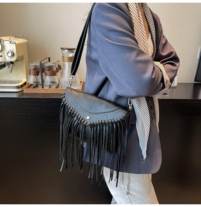 Detail view of a black leather messenger bag with tassels and woven edge on a blue suit