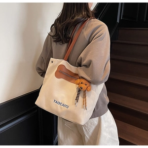 Close-up of canvas tote bag featuring brown leather handles and a cute dog plush charm