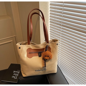 Detail of canvas tote bag featuring brown leather handles and a cute puppy plush charm