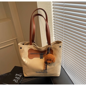 Detail of beige canvas tote with brown leather straps and a cute teddy bear charm