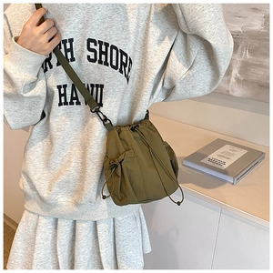 Detail of olive green nylon bucket bag featuring drawstring closure and side mesh pocket