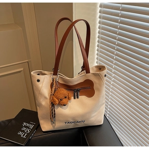 Detail of canvas tote bag with brown leather straps and cute teddy dog plush pendant