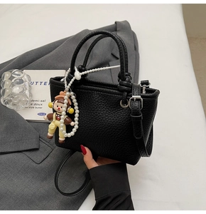 Detail of black lychee grain bucket bag featuring round handles and pearl charm