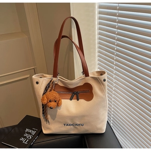 Detail of canvas tote bag with brown leather handles and teddy dog plush charm accessory