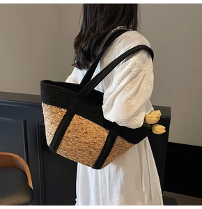Detail of hand-woven straw tote bag featuring black canvas trim and top handle strap