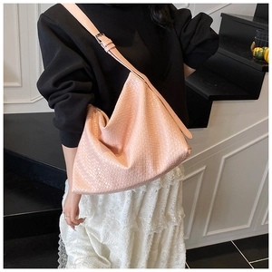 Detail of pink woven PU leather tote bag with wide strap on model in indoor setting
