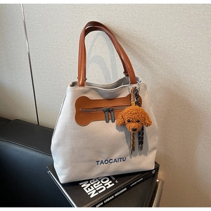 Detalle del bolso tote de lona con asas de cuero y colgante de perro de peluche