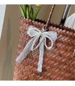 Détail d'un pendentif nœud en dentelle de perles sur un sac de plage en paille tressé