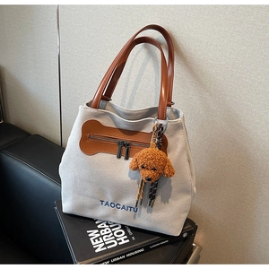Detail of grey canvas tote bag with brown leather handles and puppy charm accessory