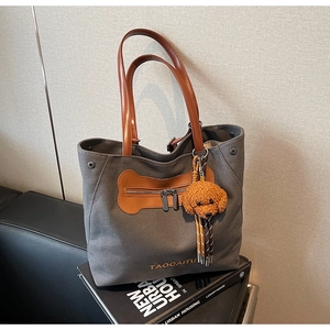 Detalle de bolso tote de lona gris con asa de cuero marrón y colgante de peluche de perro