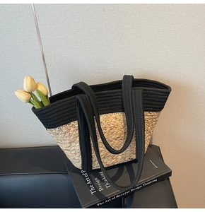 Détail du sac cabas tissé avec base en paille naturelle et anses noires en tissu