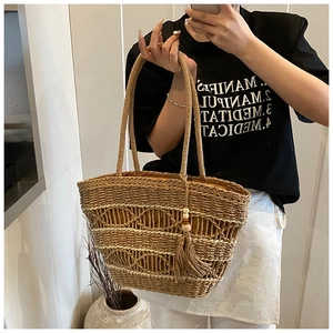 Close-up of handmade woven straw tote with white wave patterns and beaded tassel charm