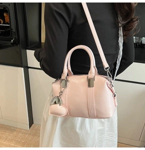 Detail of light pink patent leather boston bag with silver heart charm and chain accessory