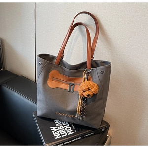 Detail of grey canvas tote bag with brown leather straps and teddy bear charm