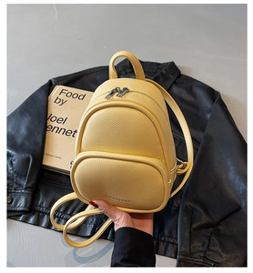 Detail of a bright yellow mini backpack in lychee pattern on a black leather jacket
