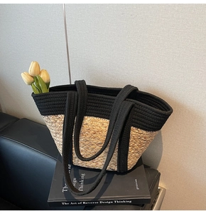 Détail d'un grand sac cabas tissé en corde noire et paille posé sur un livre de design