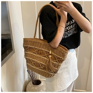 Detail of bohemian straw tote bag with intricate hollow weaving and tassel accents