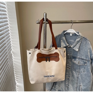 Detail of off-white canvas tote with brown leather handles and bone-shaped front pocket
