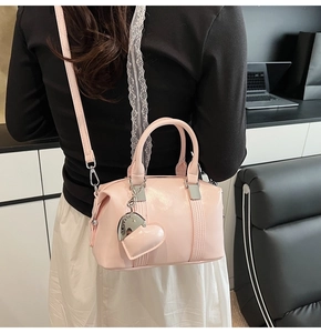 Detail of pink crossbody bag with heart pendant and silver hardware on a model