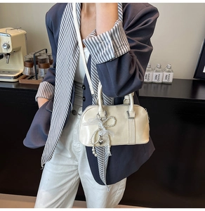 Detail der cremefarbenen Boston Bag mit glänzendem Finish und Perlenanhänger
