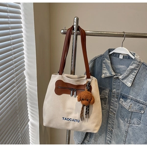 Close-up of canvas tote bag with brown leather accents and a teddy bear charm