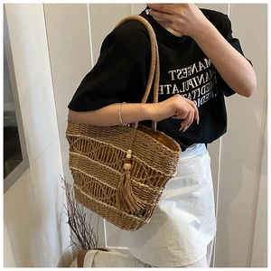 Detail of large woven straw bag with decorative tassels and wooden beads on a shoulder strap