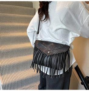 Detail of a black leather tassel crossbody bag worn by a model on a staircase