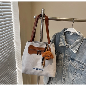 Close-up of canvas tote bag with brown leather handles, dog pendant, and logo embroidery