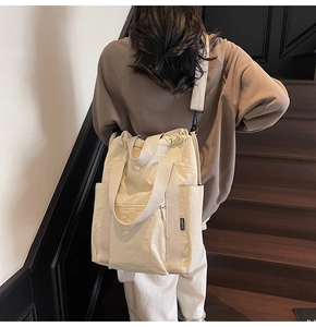 Detail of off-white nylon tote bag showing drawstring closure and metallic zipper pocket