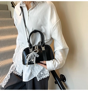 Detail einer schwarzen glänzenden Muschel-Tasche mit Spitzenschleife und Perle