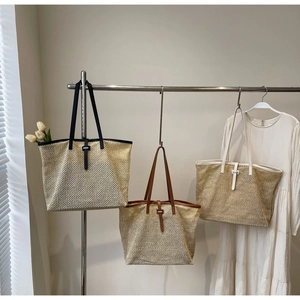 Trois sacs cabas en paille tissée de couleurs variées suspendus dans un décor minimaliste