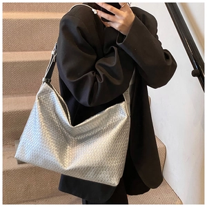 Detail of silver woven hobo tote bag with metallic texture on a model wearing a black blazer