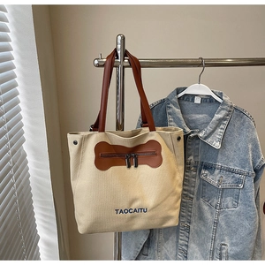 Detail of canvas tote bag showing bone-shaped pocket and leather handles on white background