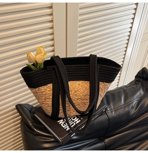 Detail of hand-woven straw tote bag with black braided rope handles and textured contrast