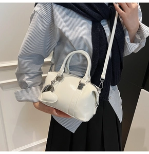Detail of a creamy white glossy patent leather handbag with a heart shaped pendant charm