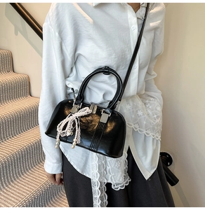 Detail der schwarzen Lackhandtasche mit Spitzen-Schleife und Perlenanhänger im Fokus
