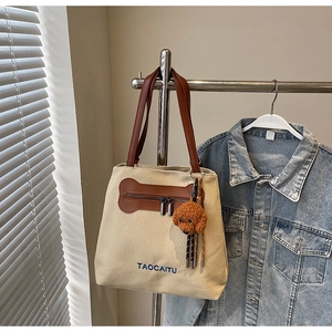 Detail of canvas tote bag with brown leather handles and a plush dog charm accessory