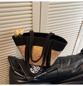 Gros plan d'un sac cabas en paille bicolore avec anses noires sur fond intérieur épuré