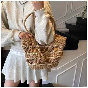 Detail of woven straw tote bag featuring tassel charms and yellow inner lining