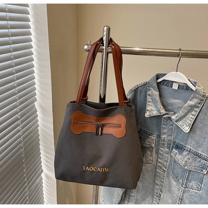 Close-up of a large grey canvas tote bag featuring brown leather trim and zipper pocket