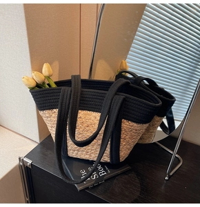 Détail d'un grand sac cabas en paille avec des anses noires sur une surface réfléchie