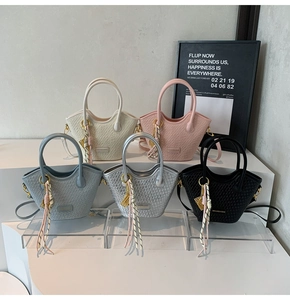 Détail de cinq sacs seaux tissés en crème, rose, bleu, argent et noir avec pompons