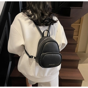 Rear view of a black mini pebbled leather backpack shown on a model in a stairwell