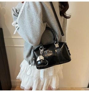 Detail of black patent leather bowling bag featuring silver heart charm and crossbody strap