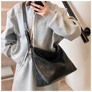 Detail of black woven tote bag with adjustable strap on a model in casual grey suit