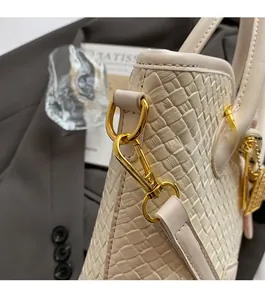 Détail du sac à main tissé crème avec ferrures dorées sur une veste de tailleur grise