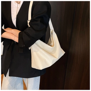 Detail of cream white tote bag with woven texture worn by a model in a black blazer