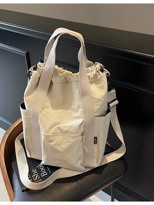 Versatile beige canvas tote bag with drawstring closure and large zipper pocket on chair