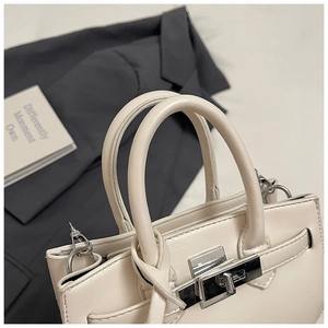 Close-up of off-white leather handbag with silver twist lock and minimalist dual handles